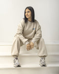Person wearing a beige tracksuit with a logo, sitting on a surface.