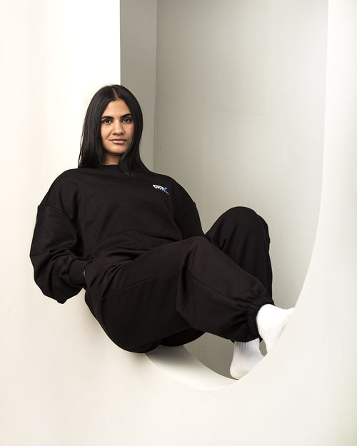 Person wearing a G3X black outfit with a logo, sitting against a background