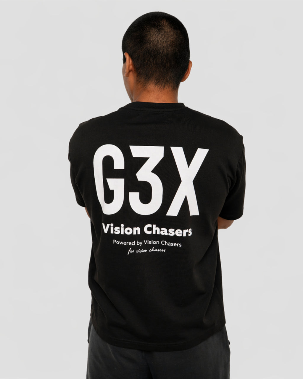 Person wearing a black t-shirt with 'G3X Vision Chasers' text on the back against a gray background