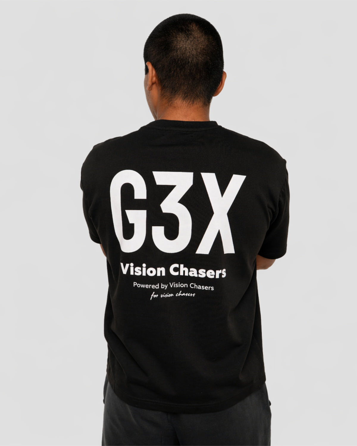 Person wearing a black t-shirt with 'G3X Vision Chasers' text on the back against a gray background