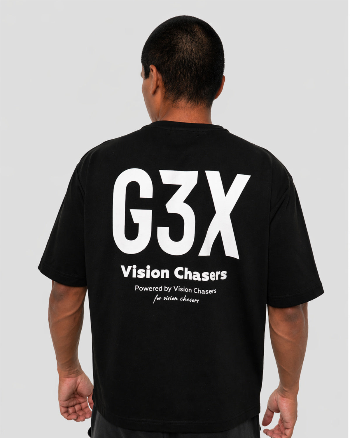 Person wearing a black t-shirt with 'G3X Vision Chasers' text on the back against a gray background