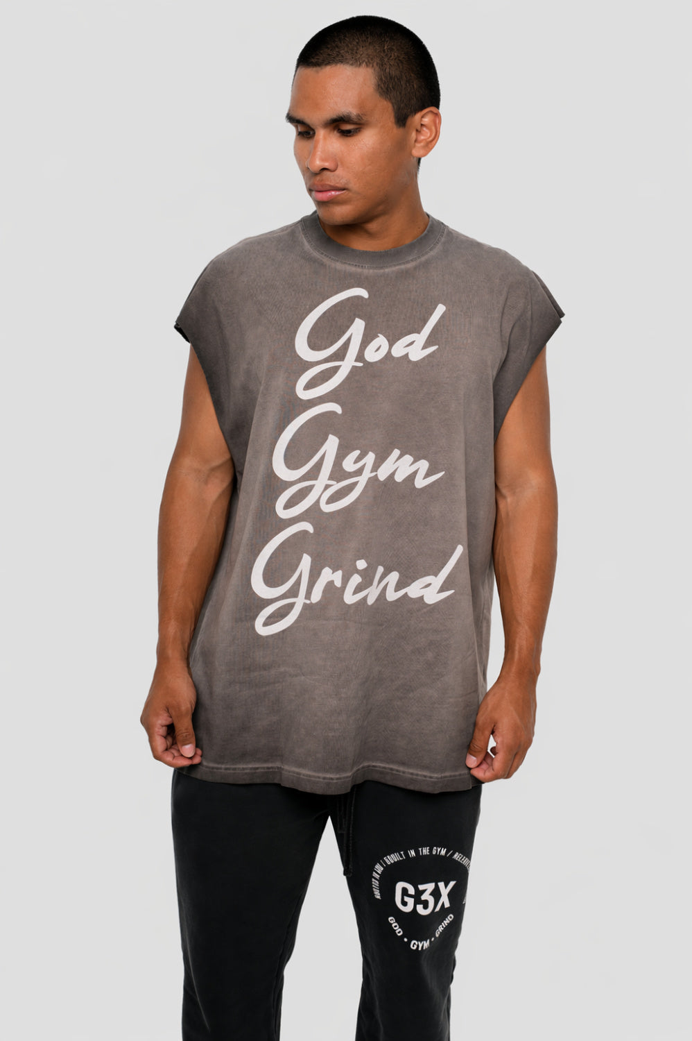 Man wearing a sleeveless gray shirt with 'God Gym Grind' text on a plain background