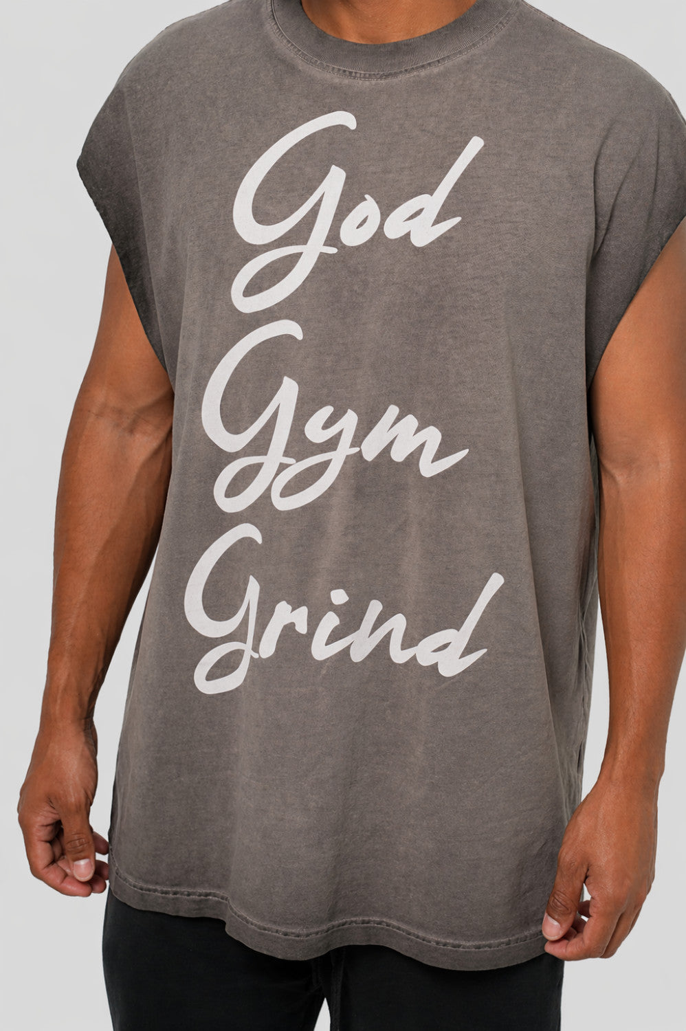 Gray t-shirt with 'God Gym Grind' text worn by a person on a plain background