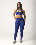 Woman wearing a medium blue sports bra and leggings set on a background
