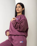 Woman wearing a plumb tracksuit with a logo on a plain background
