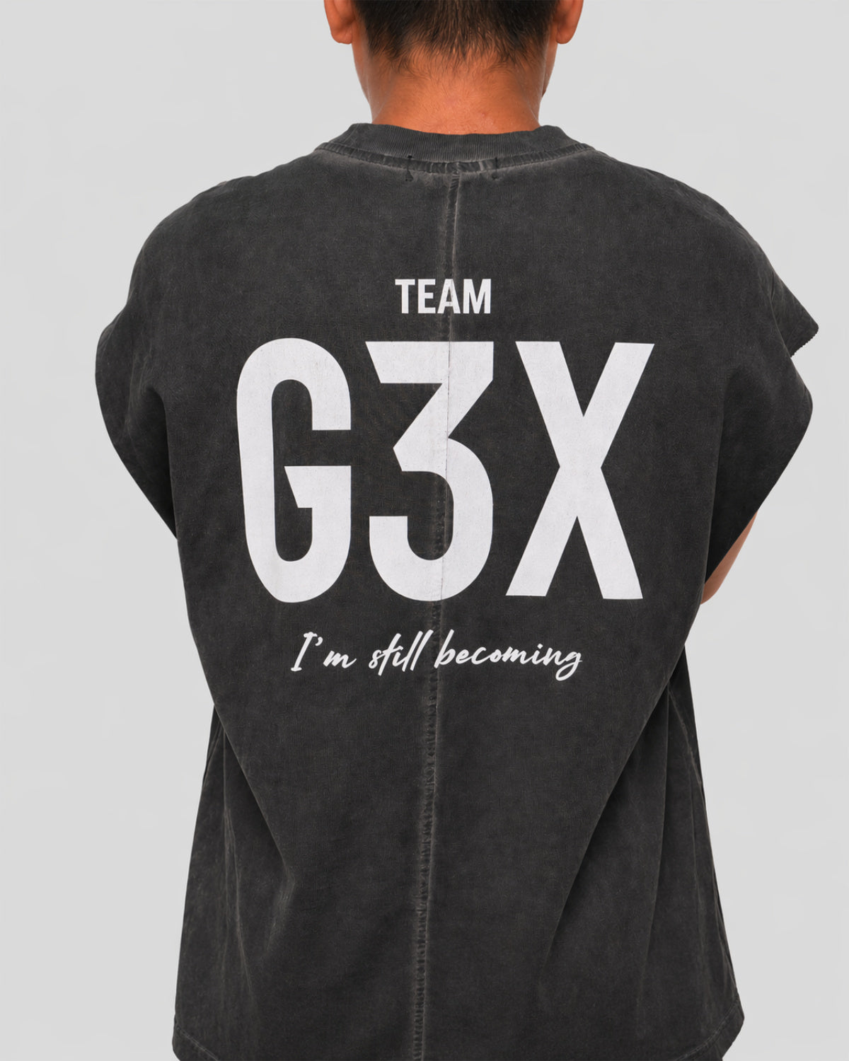 Person wearing a black shirt with 'TEAM G3X I'm still becoming' text on the back against a background